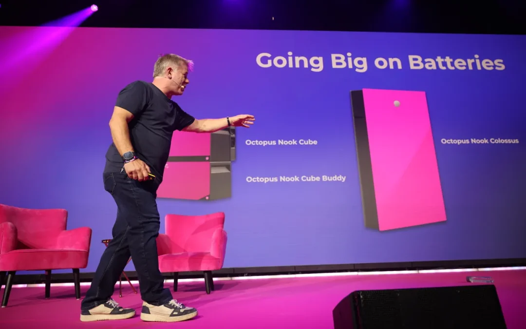 Greg Jackson on stage at the Octopus Energy Tech Summit, gesturing towards a presentation screen displaying the new pink Octopus Nook Cube and Colossus home batteries.