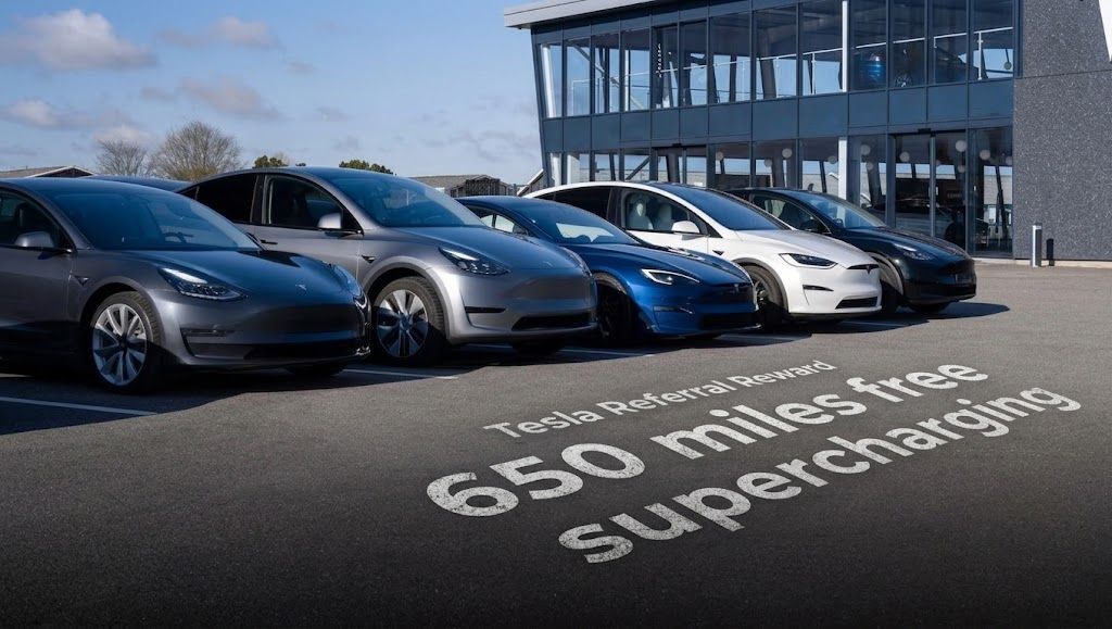 A photograph of several Tesla cars parked in front of a modern dealership. A text overlay on the asphalt pavement in the foreground reads "Tesla Referral Reward: 650 miles free supercharging".